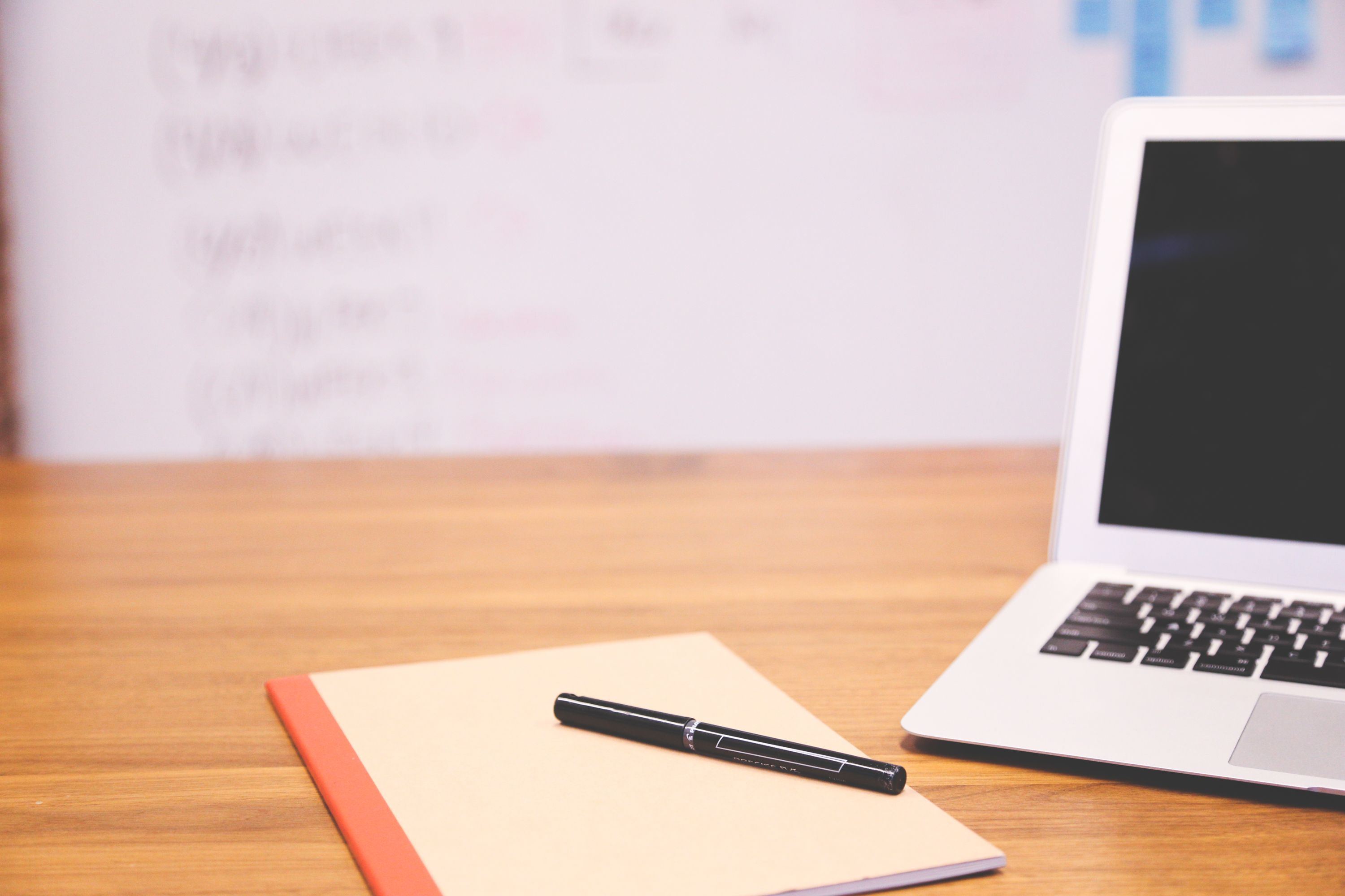 Office workspace with laptop, notebook and pen on a wooden desk